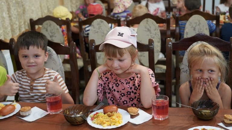 three children sitting at a table eating lunch