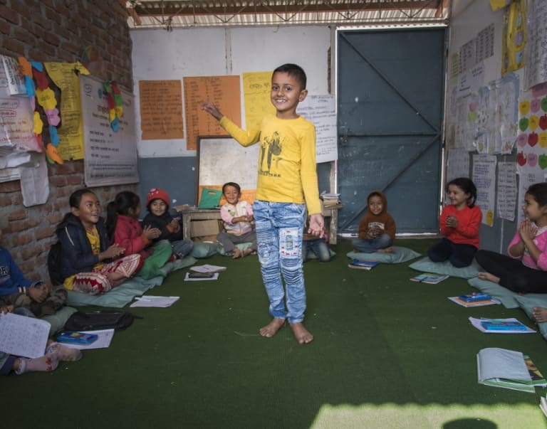 Child standing in classroom surrounded by classmates