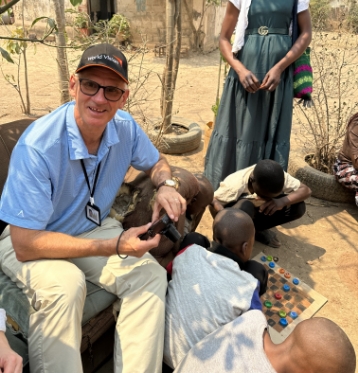 A smiling man sitting with children playing a board game in a Zambian school