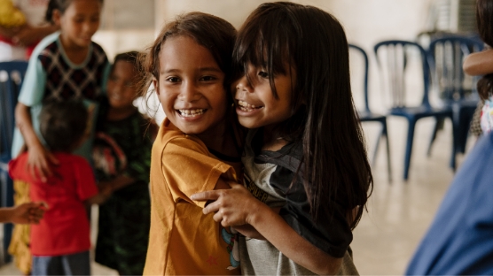 Two young girls hugging and smiling in classroom