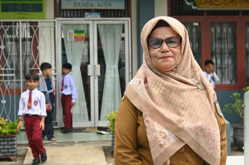 Senior teacher Darmawati standing resiliently in front of her school in Indonesia.