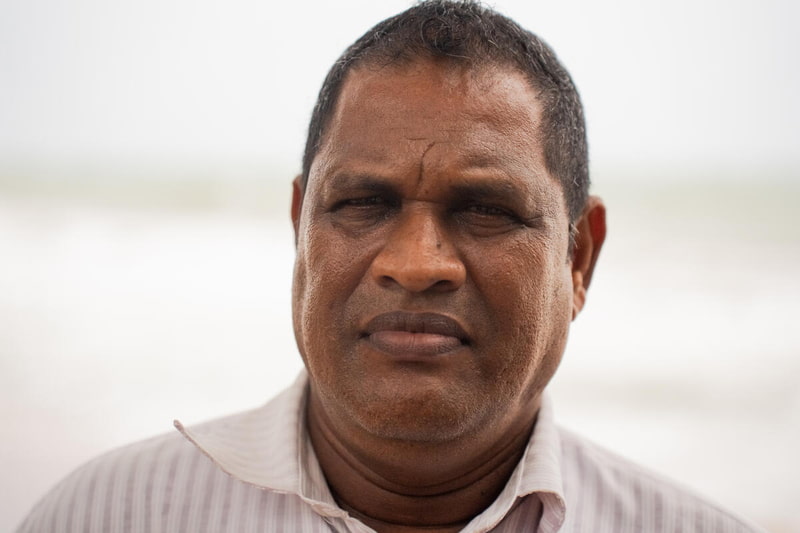 A close-up of Shantha, a tsunami survivor and fisherman from Sri Lanka, his face tense with restrained emotion.