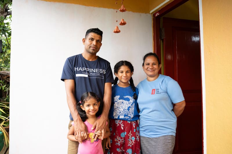Supipi, her husband and two daughters in front of a brightly painted house in Sri Lanka.