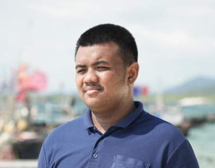A close-up of Tawan, a youth leader and sponsored child, in front of fishing boats in Thailand.