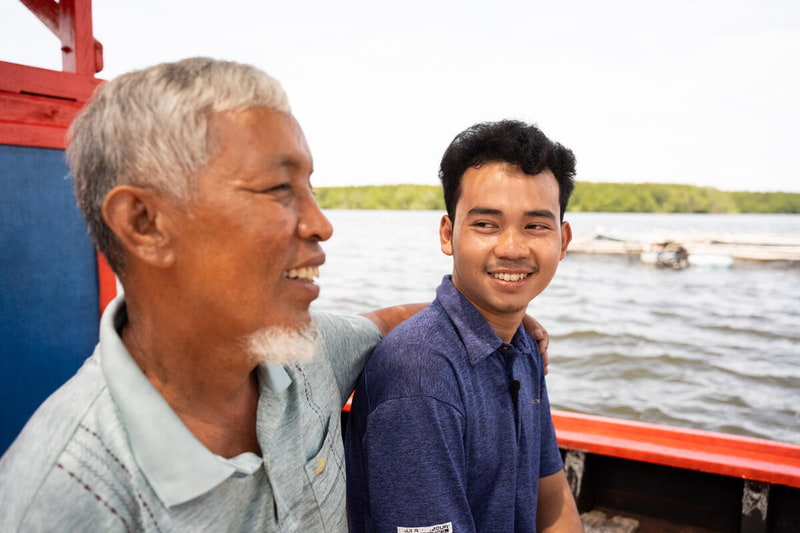 Somchai and his son laughing, arms linked, on a fishing boat in Thailand.