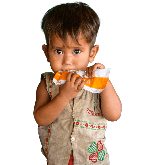 A toddler with wide brown eyes sucking on a World Vision branded packet of emergency food.