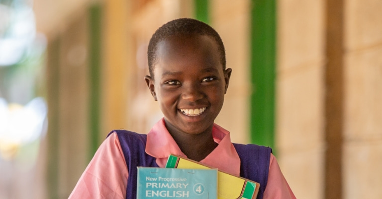 Kenyan girl in uniform smiling, holding school books
