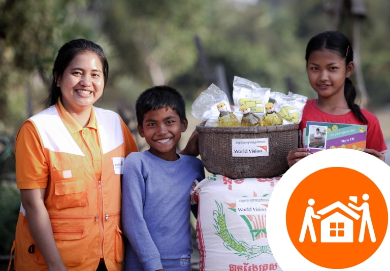 World Vision worker with two children around a basket of food
