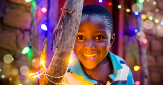 Zambian boy smiling, with Christmas lights behind him