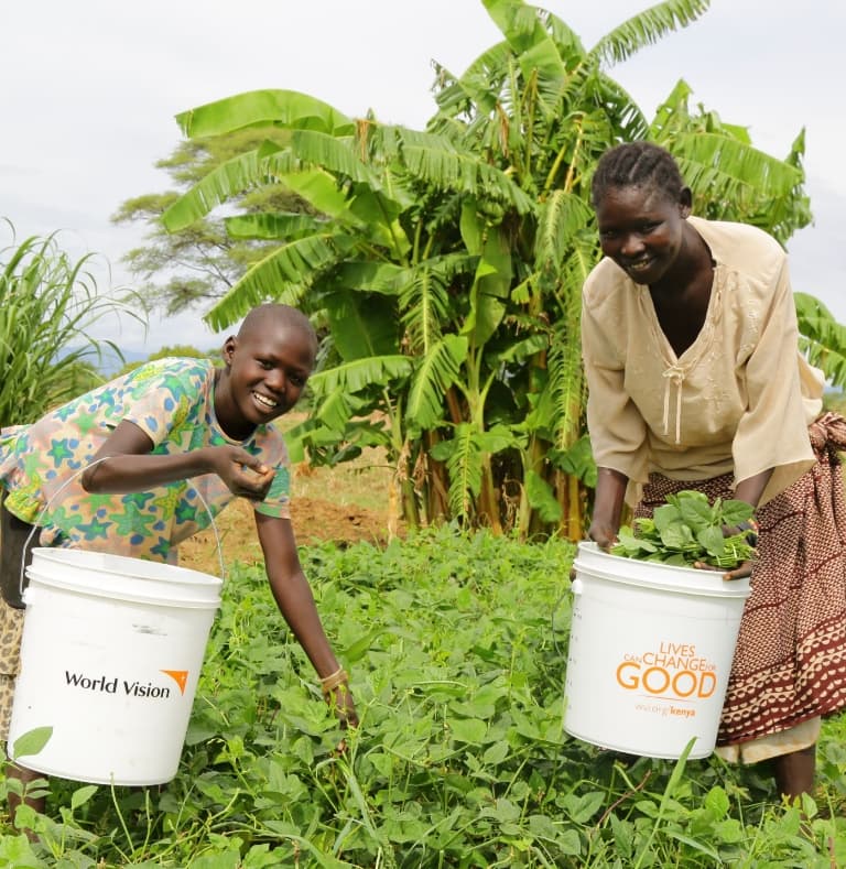 Two women picking bright green vegetables and placing them in World Vision buckets for collection