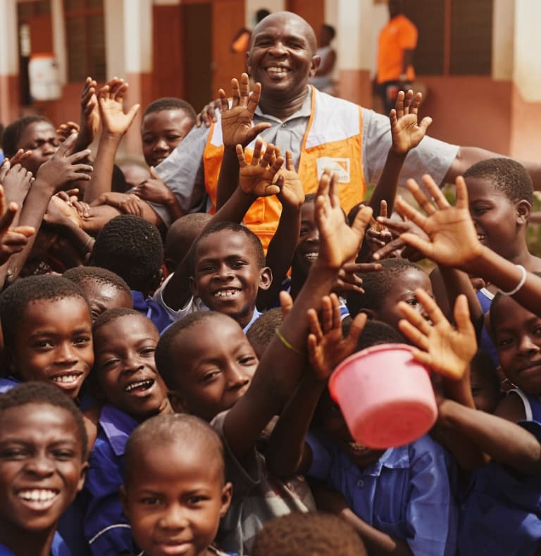 Group of young children cheering and celebrating, surrounding a World Vision worker sharing in their happiness