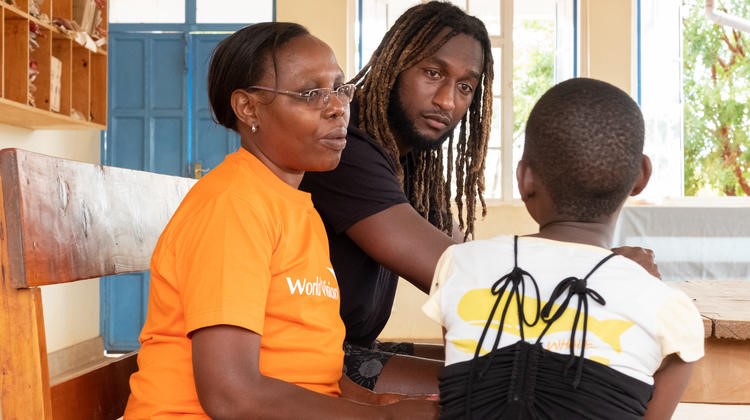 Nic Naitanui sits in a classroom with a World Vision staff member and a young girl.
