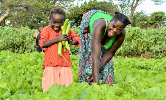 Woman and daughter in a vegetable patch smiling