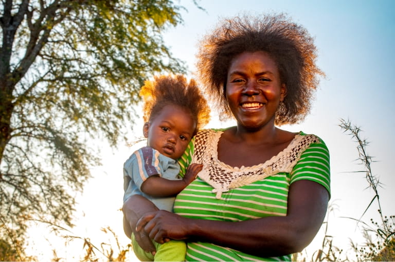 Woman with bushy hair smiling, holding a child