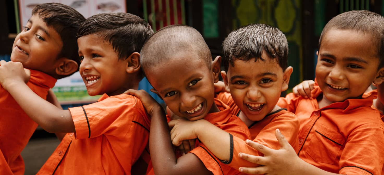 Five smiling boys in orange school uniforms standing on their side in a line