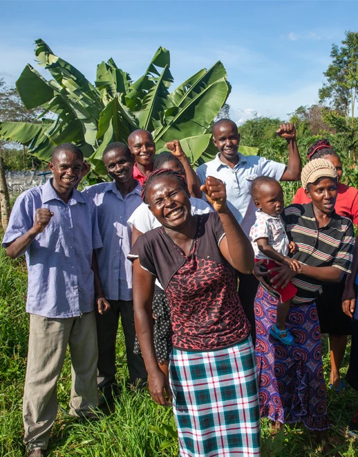 A smiling group of farmers in front of palm trees with hands raised in celebration.
