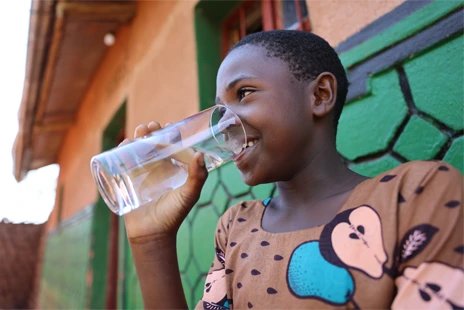 A girl smiling and drinking clean water outside.