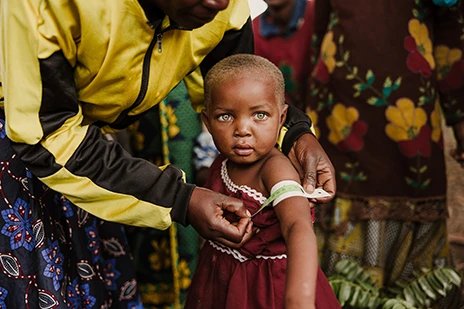 Young girl with clear green eyes having her left arm measured by an adult for heath reasons.