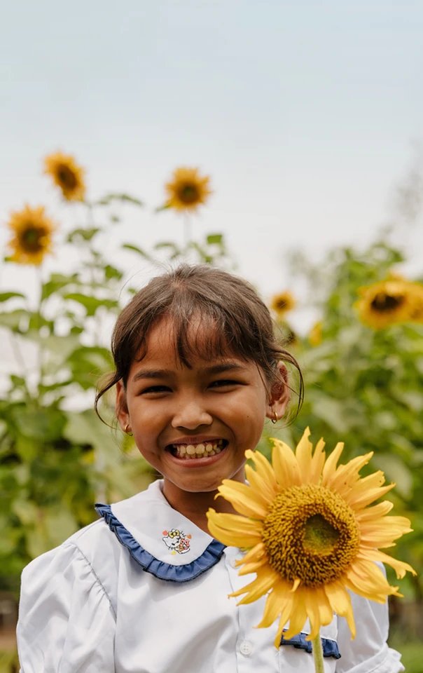 A smiling girl standing in a field and holding a sunflower.